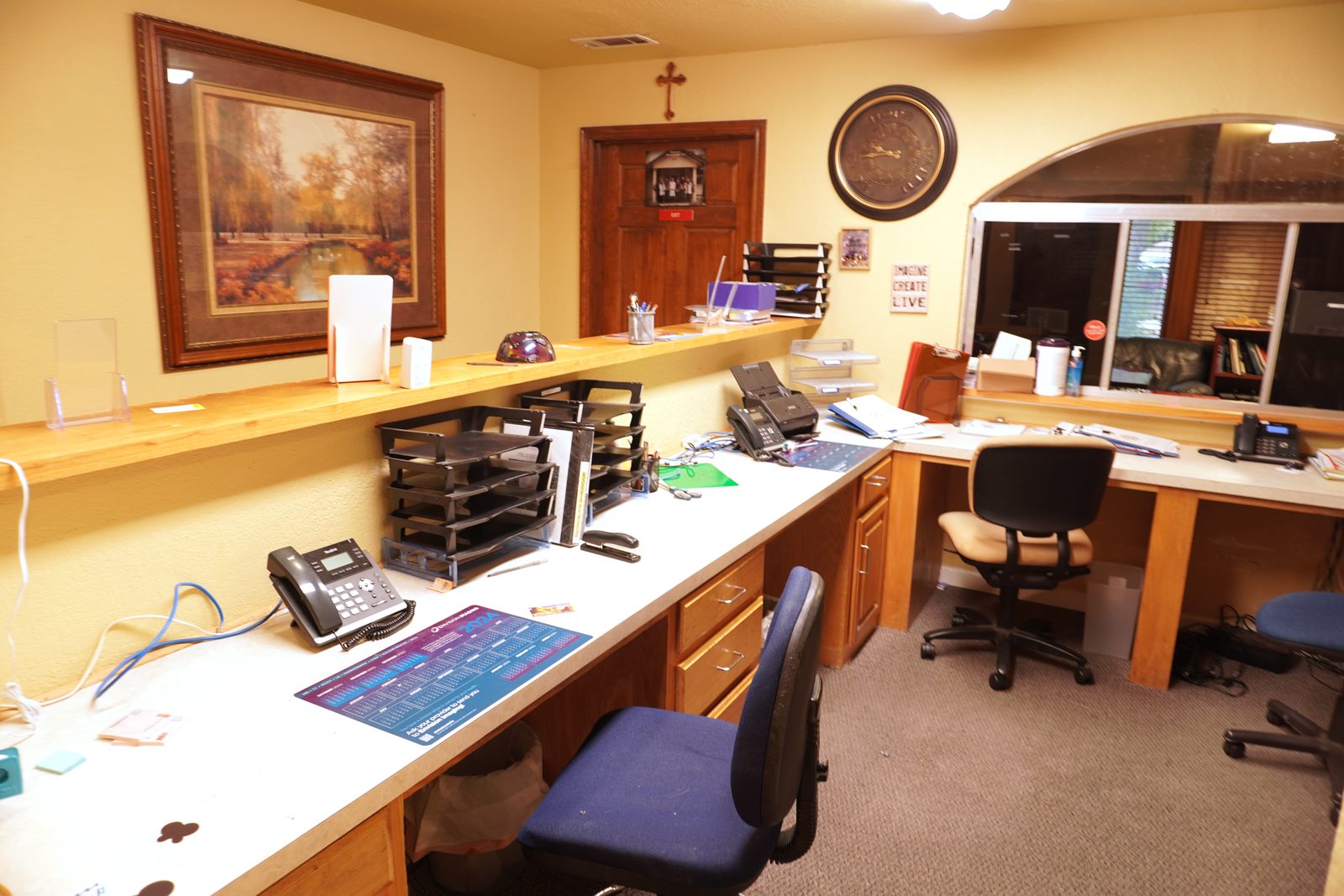 Administrative work area with an L-shaped desk, framed landscape painting and an arched pass-through window to the waiting room.