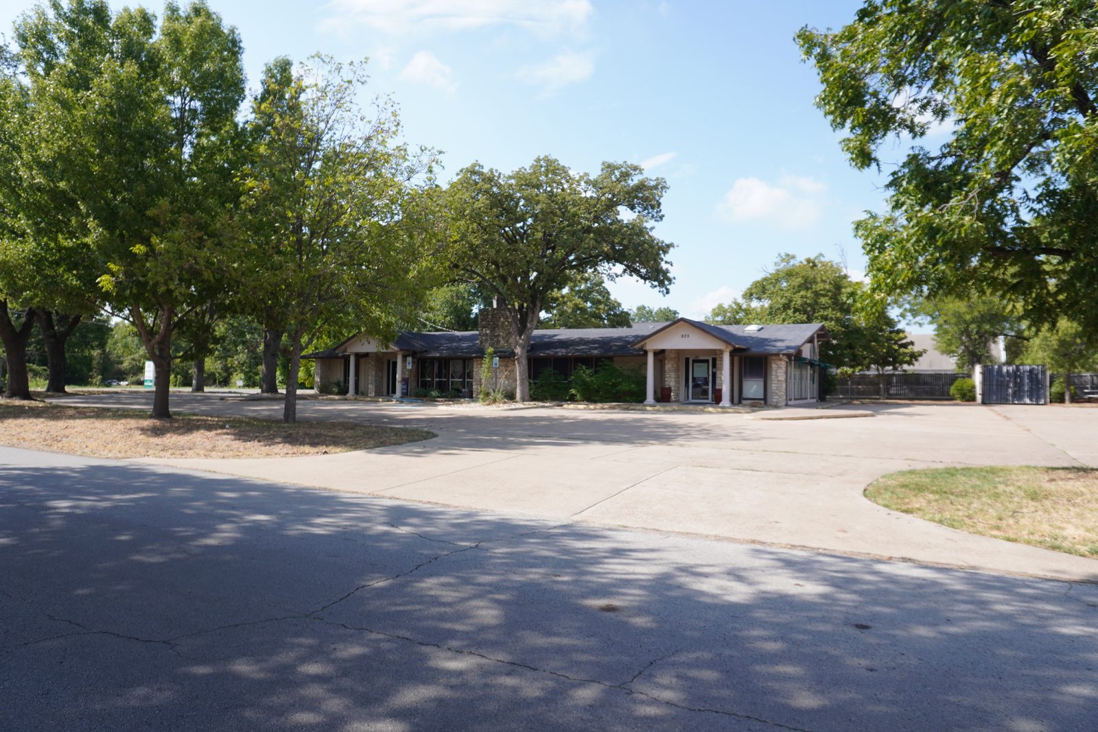 Single-storey office building seen across the front parking lot, shaded by mature trees.