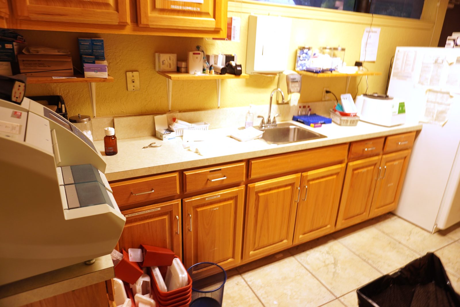 Laboratory counter run with a benchtop diagnostic analyser, specimen racks and oak cabinetry.