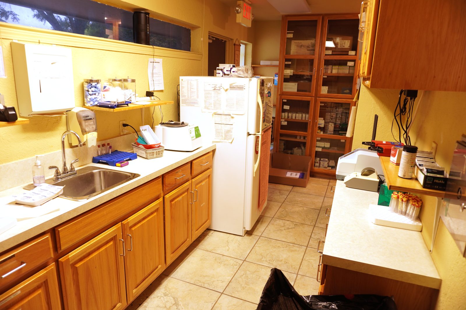 Galley laboratory with a stainless double sink, centrifuge and a floor-to-ceiling glass-door supply cabinet.