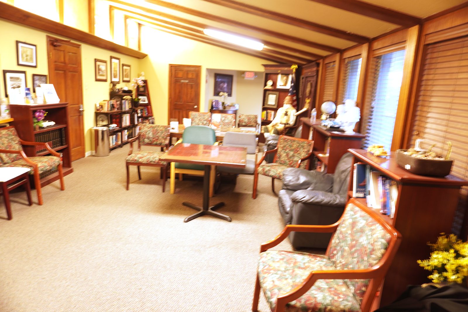 Patient library with floor-to-ceiling bookshelves, floral armchairs and a central table under wood beam ceilings.