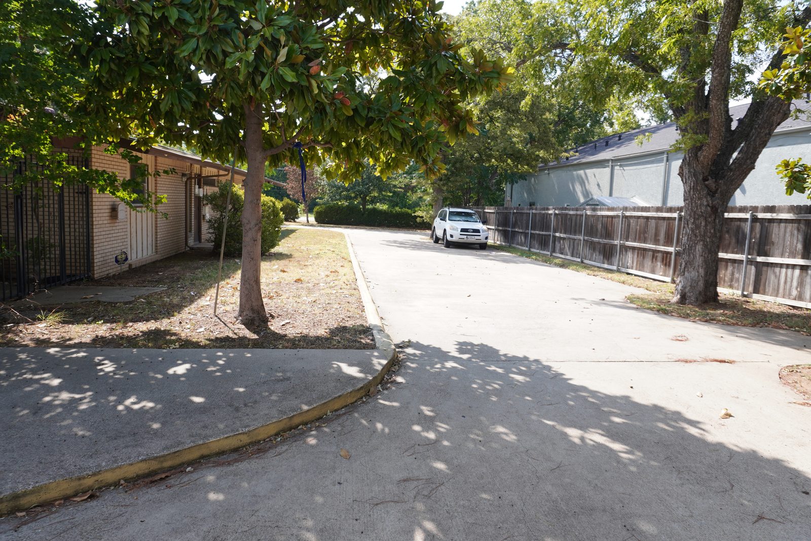 Private parking behind the building, screened by a wood fence and shaded by trees.