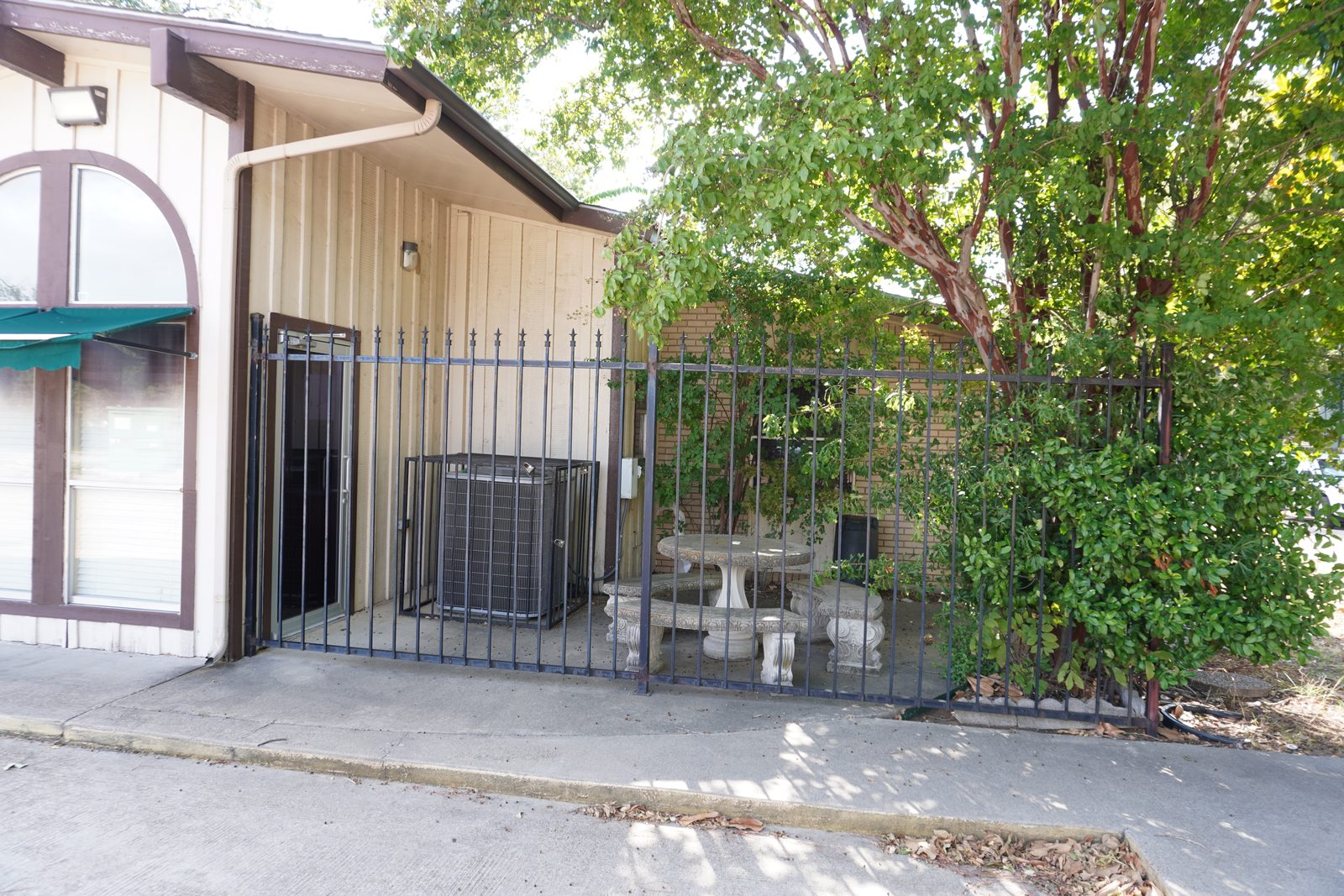 The fenced patio from outside, with a stone bistro table and seating under a crape myrtle.