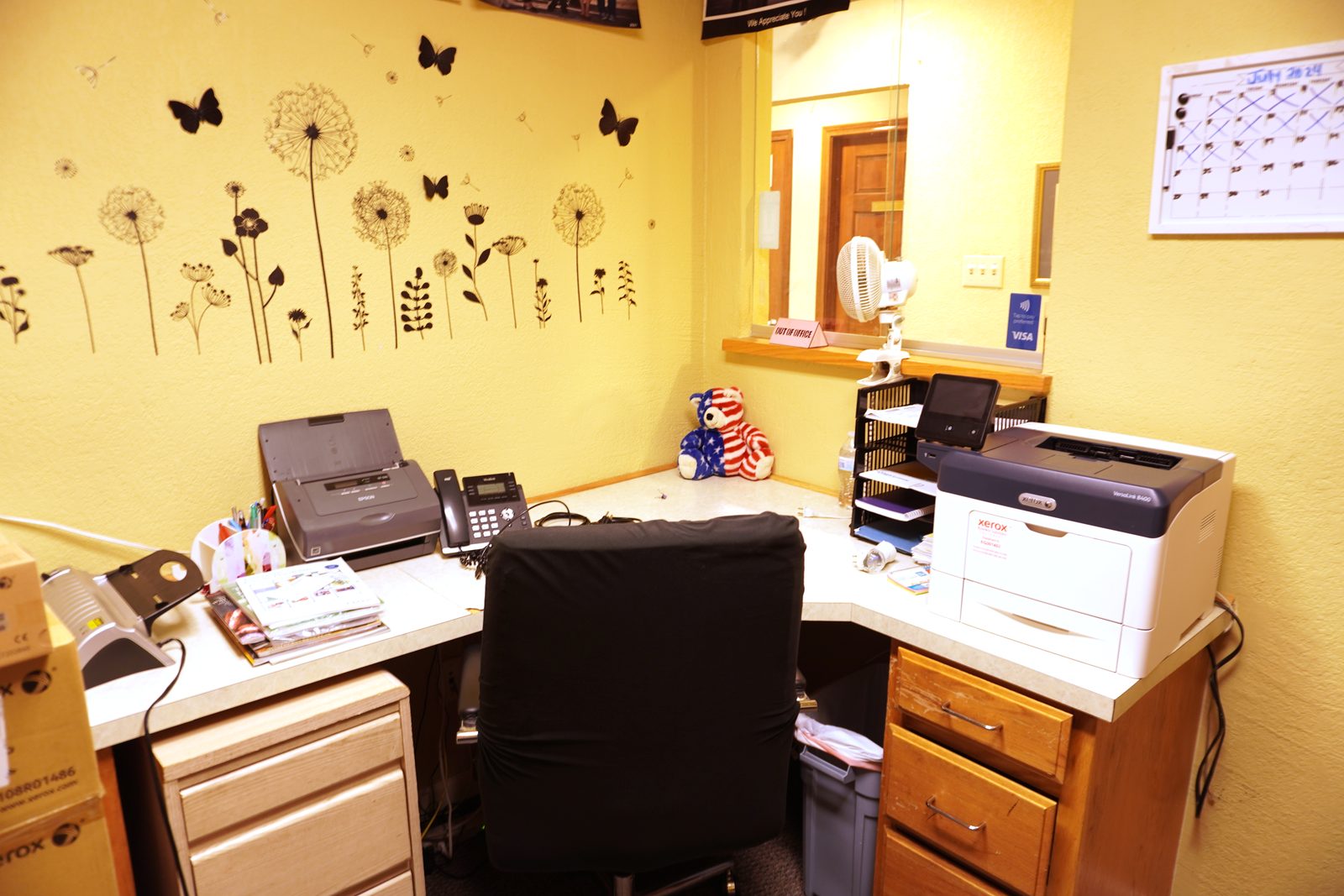 Corner staff office with an L-shaped desk and a dandelion and butterfly wall decal across the rear wall.