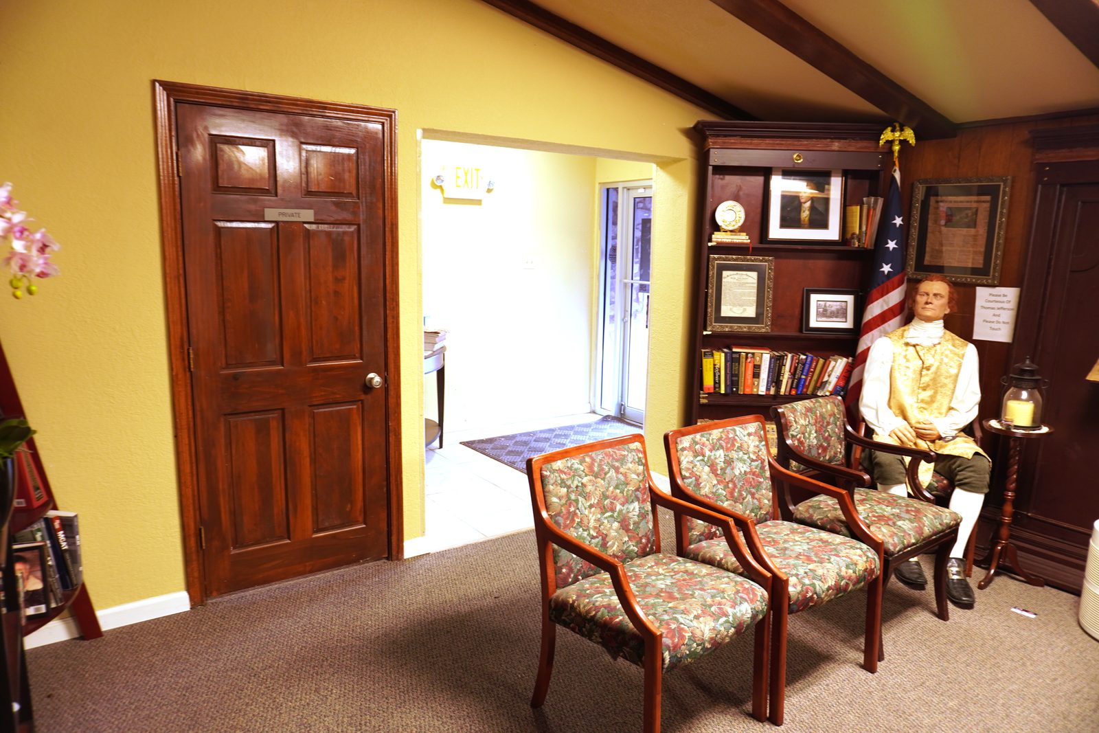 Waiting room corner with floral armchairs, exposed dark wood ceiling beams and warm yellow walls.