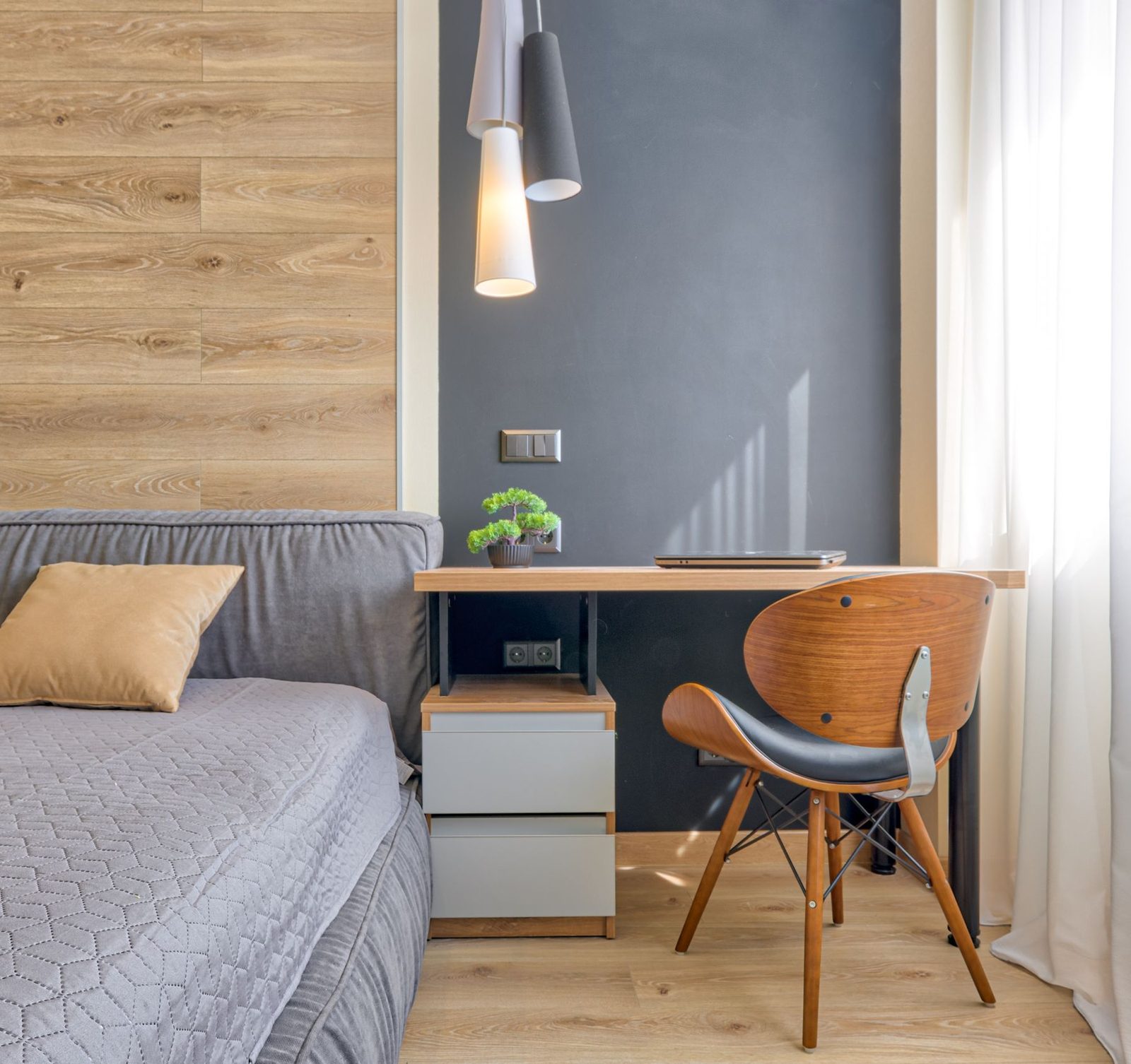 A bed beside a compact wooden desk and chair against a slate blue wall, shown as styling inspiration