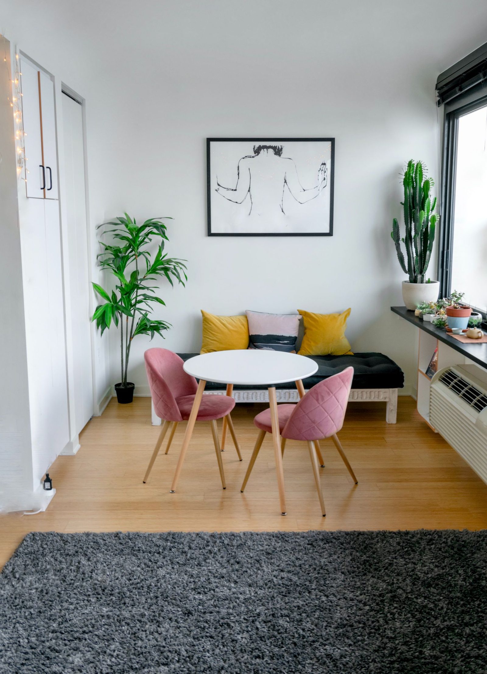 A round dining table with upholstered chairs, plants and a rug in a bright corner, shown as styling inspiration