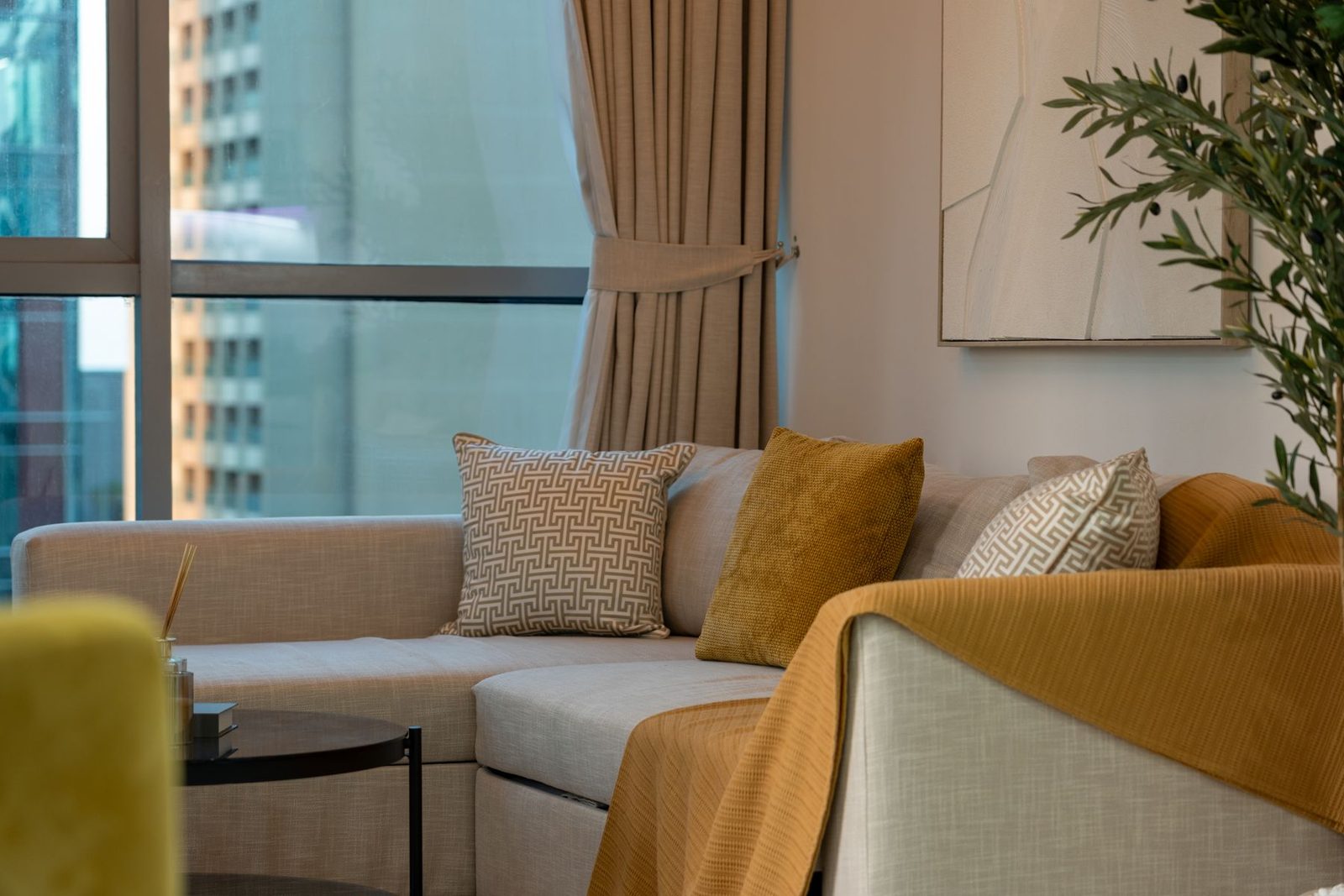 A neutral sofa with cushions and a leafy plant beside a bright window, shown as styling inspiration