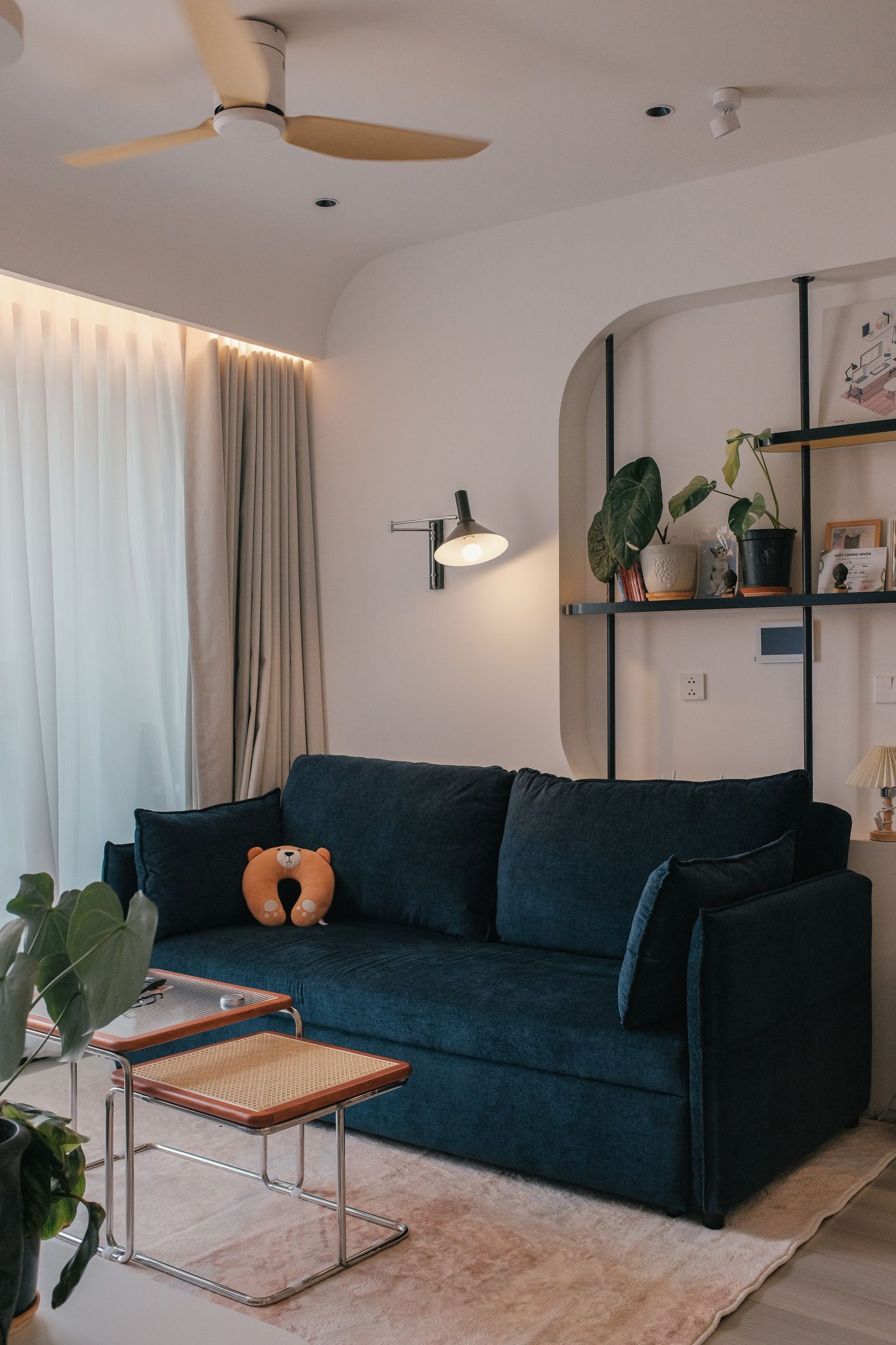 A deep blue sofa with warm lamp light and open shelving, shown as styling inspiration
